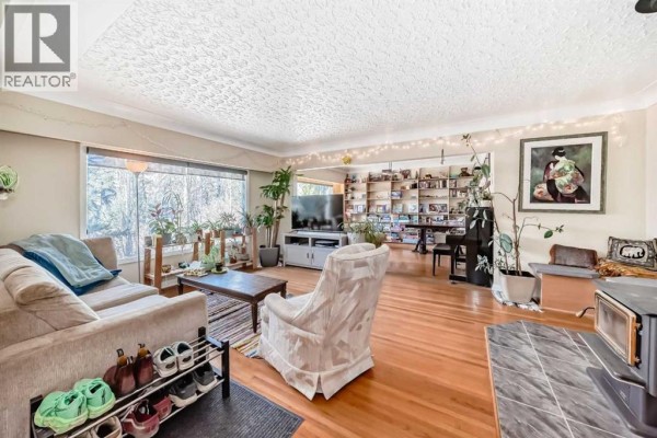 Living room with hardwood floors, beige sofa, armchair, coffee table, and large window with plants. - 2328 Capitol Hill Crescent Nw, Calgary