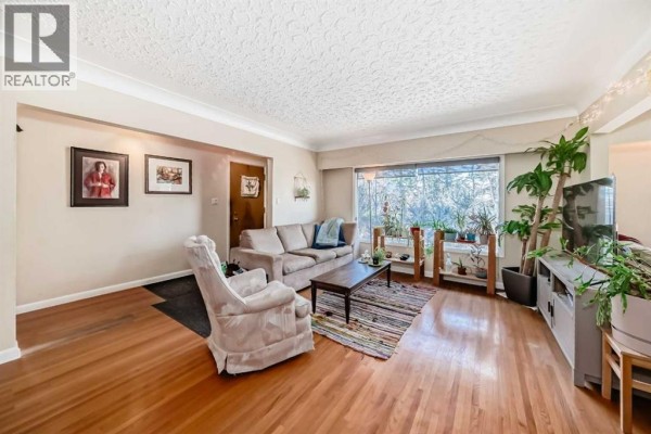 Spacious living room featuring hardwood floors, a sectional sofa, armchair, and a large window overlooking trees. - 2328 Capitol Hill Crescent Nw, Calgary