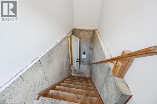 Concrete stairs with a wooden railing leading down to a white door in a basement. - 233 Dearborn Boulevard Unit# Lower, Waterloo