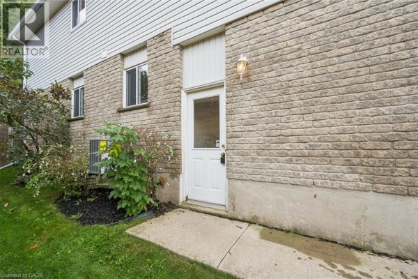 Exterior view of a brick house with a white side door and green bushes. - 233 Dearborn Boulevard Unit# Lower, Waterloo