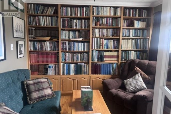 Wall-to-wall wooden bookshelves filled with books, with a blue sofa and brown armchair. - 233 Elizabeth Drive, Gander