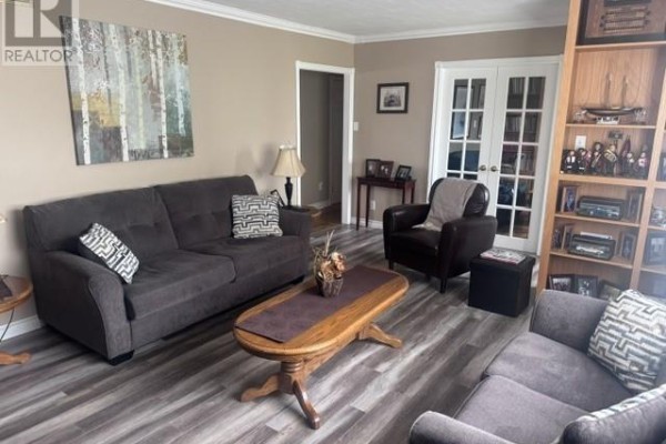 Living room with a dark grey sofa, brown armchair, coffee table, and grey wood-look flooring. - 233 Elizabeth Drive, Gander