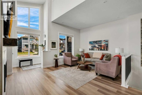 Living room with light wood floors, pink chairs, a grey sofa, and a large window with a view. - 233 Haskayne Drive Nw, Calgary