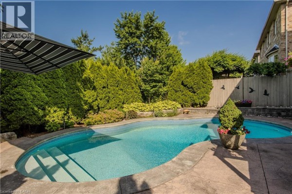 View of a swimming pool with a patterned umbrella and manicured hedges in the backyard. - 2330 Valleyridge Drive, Oakville