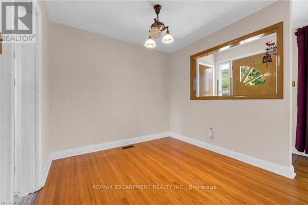 Spacious living area with hardwood floors, cream walls, large windows with burgundy curtains, and a decorative mirror. - 234 Pine Cove Road, Burlington