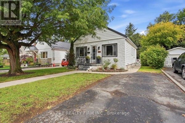 Side view of the white brick bungalow showing the driveway, lawn, and surrounding trees. - 234 St Julien Street, London East