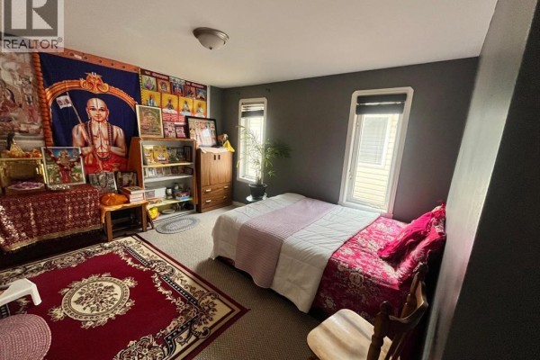 Bedroom with dark grey walls, carpet, a bed with pink bedding, and religious wall hangings. - 2349 Tranquility Avenue, Windsor