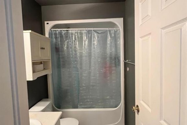Bathroom with a white bathtub and shower curtain, a toilet, and a white cabinet on the wall. - 2349 Tranquility Avenue, Windsor