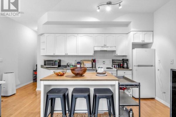 Kitchen with white cabinets, stainless steel appliances, and a wooden island with stools. - 235 - 231 Fort York Boulevard, Toronto
