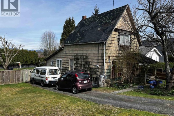Close-up exterior view of the house's wood siding and a slanted roof, with vehicles parked on the grass and driveway. - 235 Durham Street, New Westminster