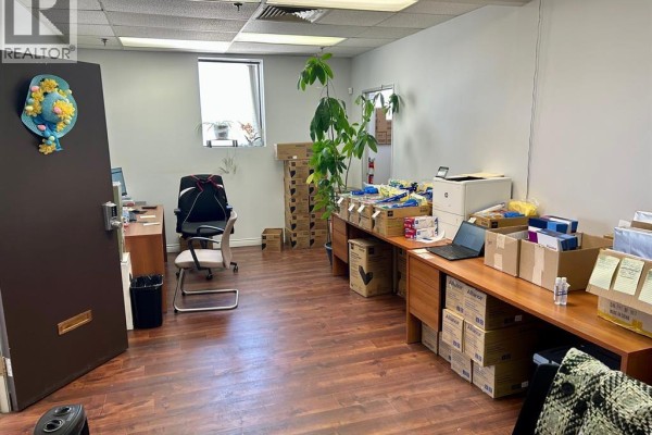 An office space with desks, chairs, boxes, and a plant, looking towards a window and a door. - 235 Eugenie Street West Unit# 208, Windsor