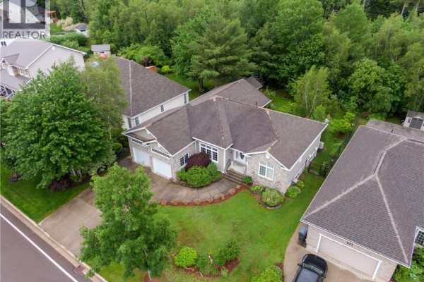 Front view of a residential house with landscaping and trees. - 235 Summerhill Row, Fredericton
