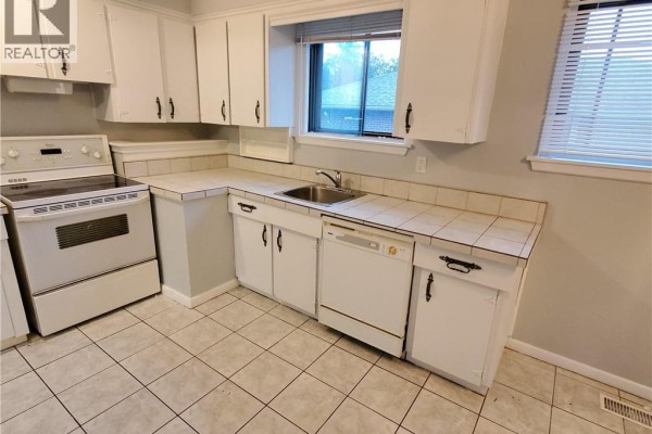 Kitchen with white cabinets, white appliances, tiled floors, and a window with blinds. - 235 Wilson Road N Unit# 1, Oshawa