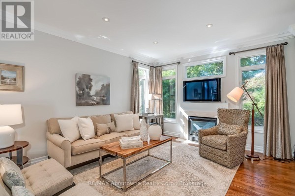 Living room with a beige sectional sofa, armchair, fireplace, and hardwood floors. - 2351 Woodfield Road, Oakville
