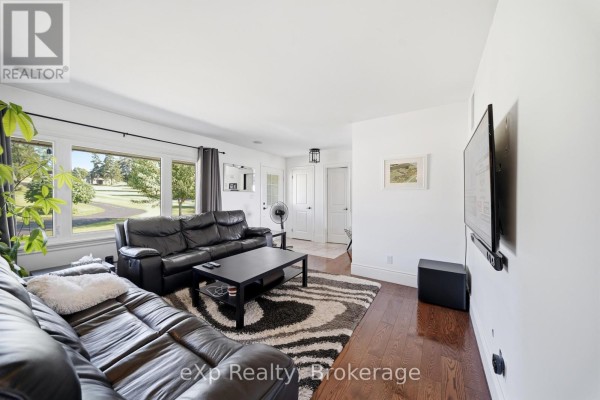 Living room with black leather sofas, a black coffee table, zebra print rug, and large windows overlooking lawn. - 2352 County Road 3, Prince Edward County