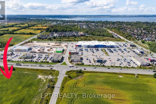 Red arrow points to a green field of crops in the foreground with a commercial plaza in the background. - 2359 Glenwoods Avenue, Georgina