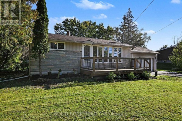 Side view of a single-story house with a wooden deck, attached garage, and lawn. - 236 Campbell Drive N, Mcnab/braeside