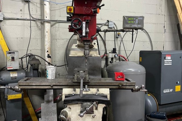 A red metal milling machine with a drill bit centered, surrounded by air compressors and equipment. - 236 Canarctic Drive, Toronto