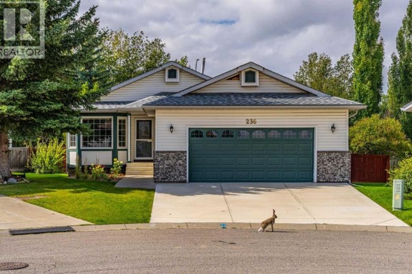 Front exterior of a beige house with a dark green garage door and green lawn. - 236 Edgebrook Gardens Nw, Calgary