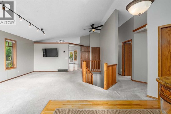 Spacious living room with vaulted ceilings, light grey walls, carpet, and wooden railings. - 236 Edgebrook Gardens Nw, Calgary