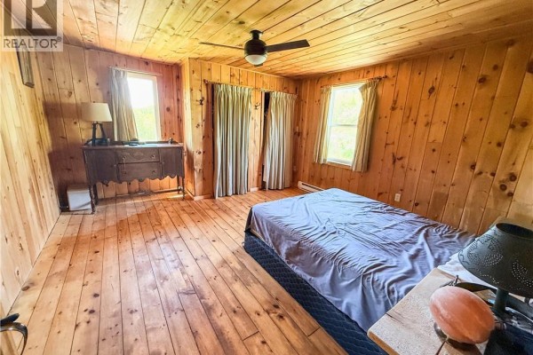 Side view of a log cabin featuring a glass sunroom and wooden deck on a grassy slope. - 236 Mill Brook Road, Mill Brook
