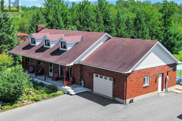 Exterior view of a red brick house with a white garage door and large windows. - 2362 Russland Road, Russell