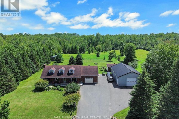 Wide aerial shot showing a house, pool, outbuildings, and expansive wooded property. - 2362 Russland Road, Russell
