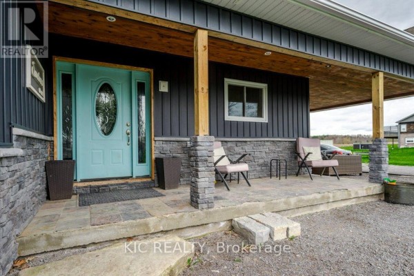 Close-up of a blue front door with glass inserts, porch with stone pillars, and outdoor seating. - 2366 Asphodel 10th Line, Asphodel Norwood