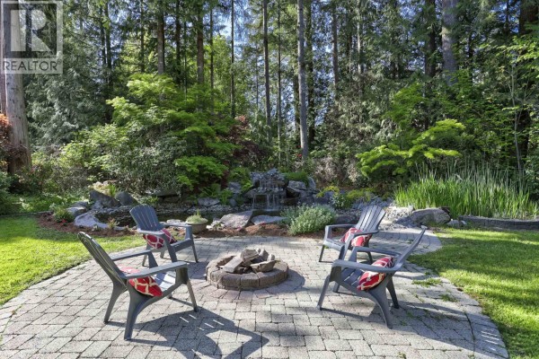 Paved patio with fire pit and four chairs, surrounded by lush greenery and trees. - 23669 128 Crescent, Maple Ridge