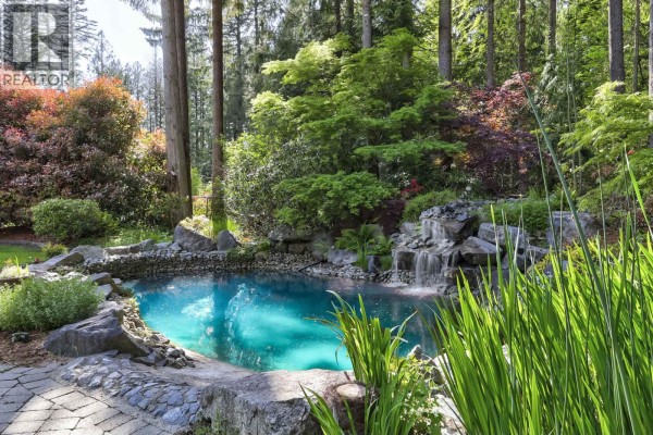 Circular pond with a small waterfall, stone edging, and tall green reeds in front. - 23669 128 Crescent, Maple Ridge