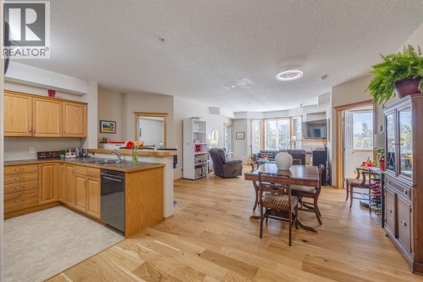 Open-concept living space with hardwood floors, oak kitchen cabinets, dining table, and living room. - 237, 15 Everstone Drive Sw, Calgary