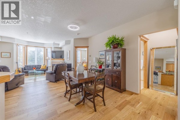 Living room with fireplace and seating area, dining area with wooden table, and hallway entry. - 237, 15 Everstone Drive Sw, Calgary