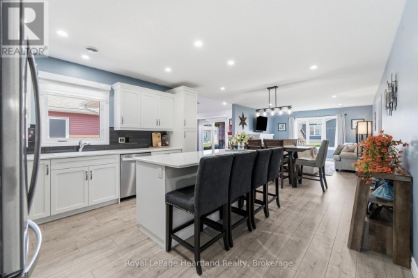 Open-concept kitchen and dining area with white cabinets, island seating, and a living room view. - 237 Lake Breeze Drive, Ashfield Colborne Wawanosh