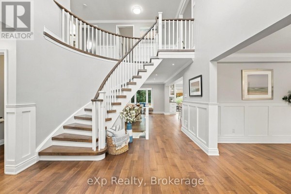 Grand foyer with a curved staircase, hardwood floors, and white wainscoting. - 237 Lake Driveway W, Ajax