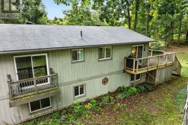 Side view of the house with a wooden deck, balcony, and surrounding greenery. - 237 Old River Road, Leeds And The Thousand Islands