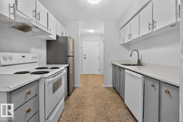Kitchen view from other end showing stove, sink, cabinets, and hallway door. - 237 Woodvale Rd Nw, Edmonton