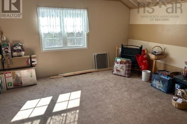 A room with tan carpet, tan walls, and a window with white lace curtains and sunbeams. - 2379 Upper Clyde Road, Clyde River