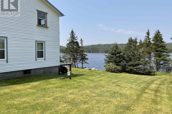 Side exterior of a white house with green lawn and calm blue water in the background. - 238 Cole Harbour Village Road, Cole Harbour