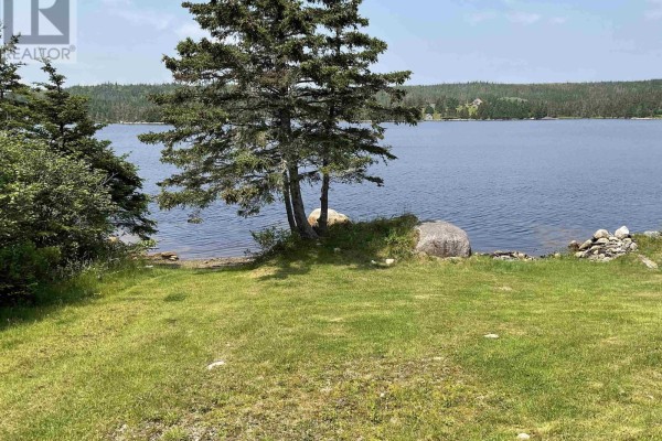 Shoreline with grass, rocks, and trees on the edge of a large blue lake. - 238 Cole Harbour Village Road, Cole Harbour