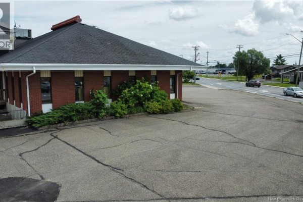 Corner of a commercial building with red brick walls, green bushes, and a street view. - 238 Madawaska Road, Grand Sault/grand Falls