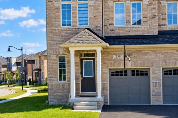 Close-up of the entrance to a beige brick townhouse with a black door and grey garage doors. - 238 Skinner Road, Hamilton