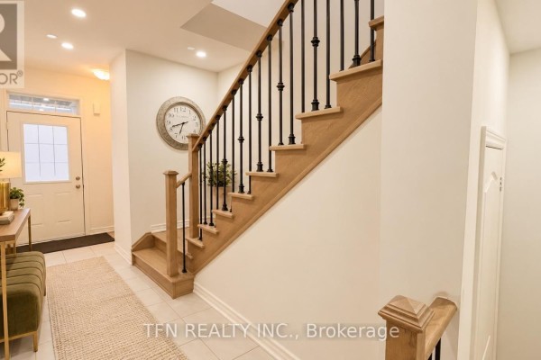 Hallway featuring a wooden staircase with black spindles, a large clock, and a light-colored rug. - 238 Skinner Road, Hamilton