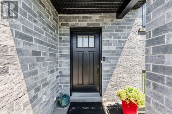 Close-up of the black front door with a frosted glass pane, surrounded by grey brick. - 2389 Watson Crescent, Cornwall