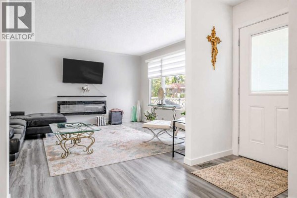 Living room with a black sectional couch, fireplace, and large window with blinds. - 239 2 Street E, Brooks