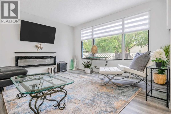 Living room with a fireplace, mounted TV, modern furniture, and large windows overlooking the yard. - 239 2 Street E, Brooks