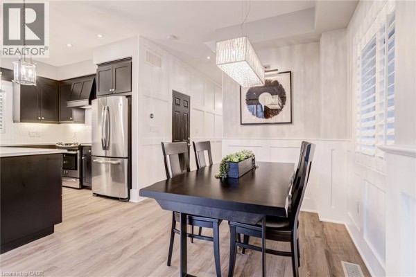 Dark wood dining table and chairs, wainscoting, modern chandelier, and kitchen - 239 Cranbrook Street Kitchener