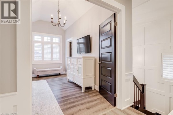 Hallway with vaulted ceiling, dark wood door, white dresser, TV, bench, and shutters - 239 Cranbrook Street Kitchener
