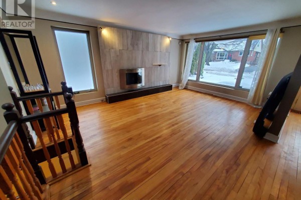 Spacious living room with large windows, hardwood floors, and a modern fireplace feature. - 239 Dale Avenue, Ottawa