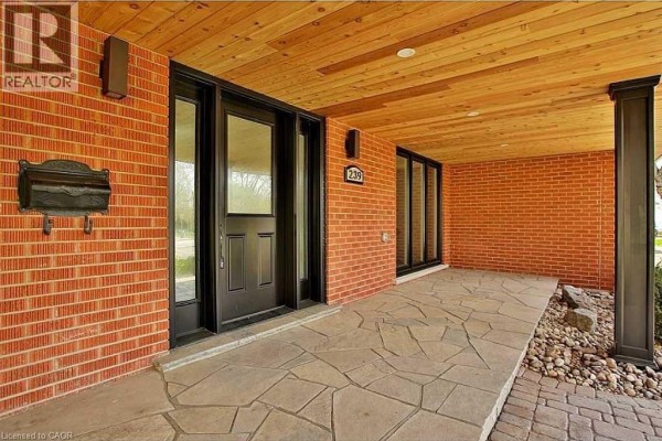 Covered front porch with flagstone flooring, brick walls, and a black front door. - 239 Guelph Line, Burlington