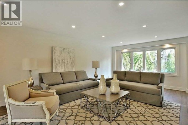 Living room with two grey sofas, an armchair, a coffee table, and a large window. - 239 Guelph Line, Burlington